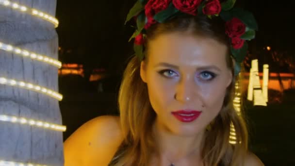 Flicka poserar mot lätta girlanger i park — Stockvideo