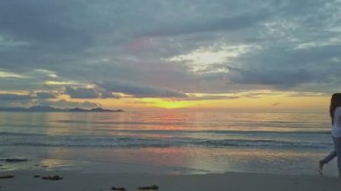 kız üzerinde kum plaj güneş doğarken yürür.