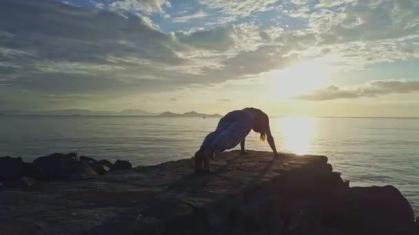 Meisje doet yoga op rotsachtige strand — Stockvideo
