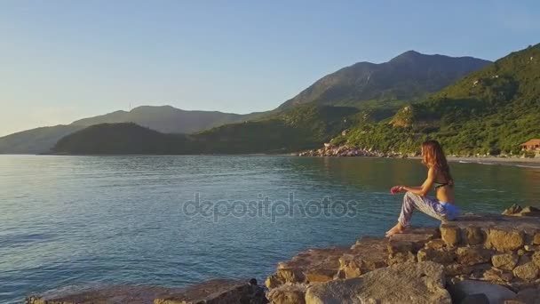 少女は、ビーチに座っているし、海の景色を楽しんでいます — ストック動画