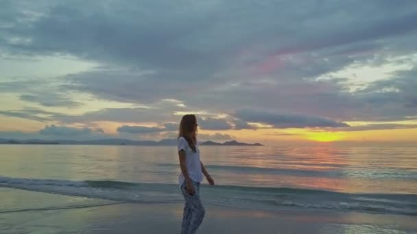 Девушка гуляет по песчаному пляжу на рассвете — стоковое видео