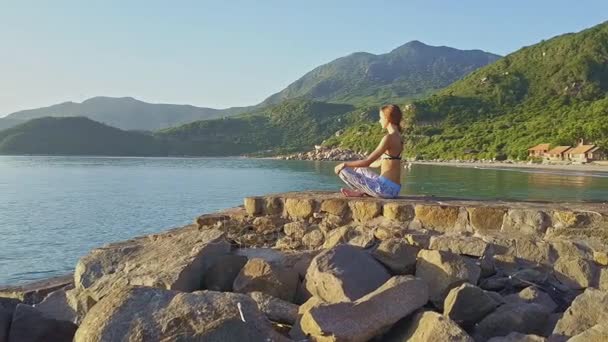 Meisje doet yoga op rotsachtige strand — Stockvideo