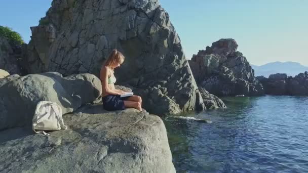 Niña leyendo libro en la costa de roca — Vídeo de stock