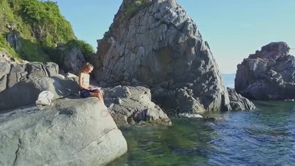 Girl reading book on rock coast — Stock Video