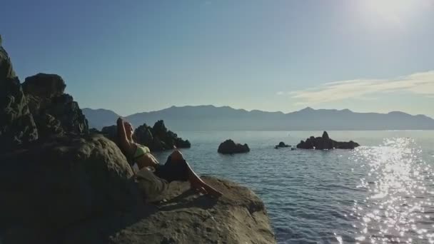 Chica apoyada en piedra contra el paisaje marino — Vídeo de stock