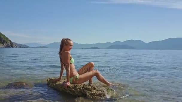 Девушка, сидящая на скале в море — стоковое видео