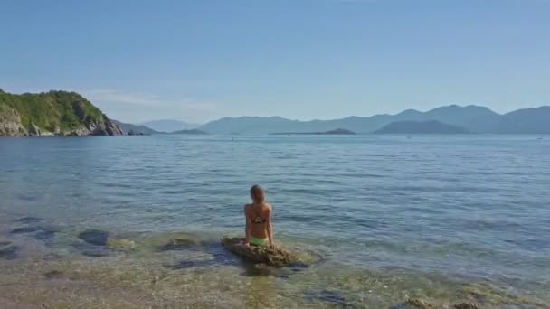 Flickan sitter på sten i havet — Stockvideo