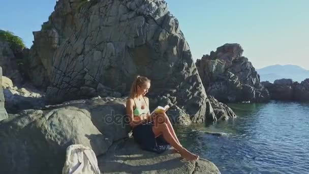 Niña leyendo libro en la costa de roca — Vídeo de stock