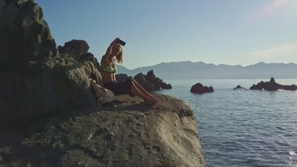 Chica tomando fotos en piedras contra el mar — Vídeos de Stock