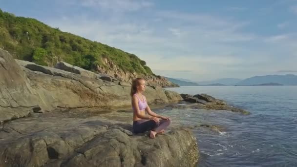 Девушка занимается йогой на скалистом побережье океана — стоковое видео