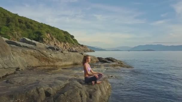 Девушка занимается йогой на скалистом побережье океана — стоковое видео