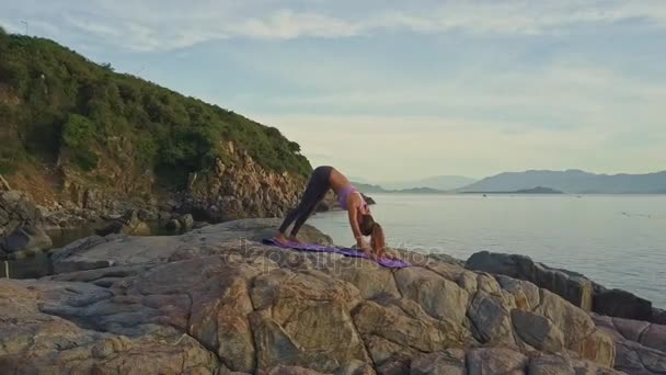 Дівчина робить йогу на скелястому узбережжі океану — стокове відео