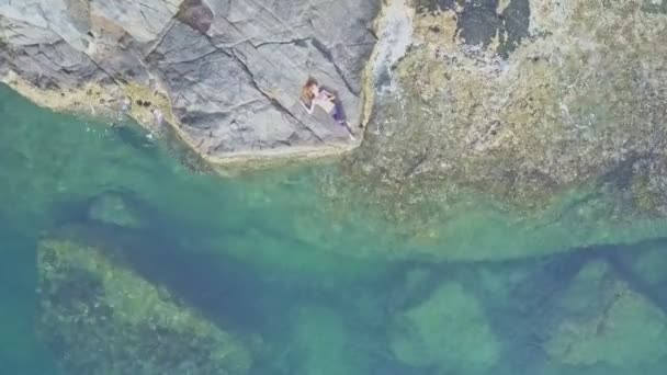 Meisje ligt op rotsachtige strand onder zonnestralen — Stockvideo