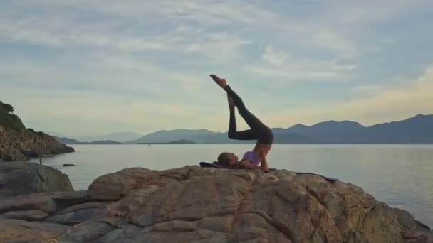 Gadis melakukan yoga di pantai berbatu laut — Stok Video