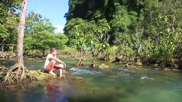 Muž sedící pod vodní toky mezi mangrovové kořeny — Stock video