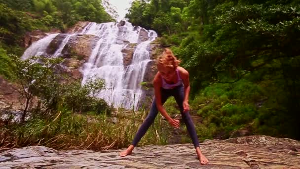 Женщина занимается йогой возле водопада — стоковое видео