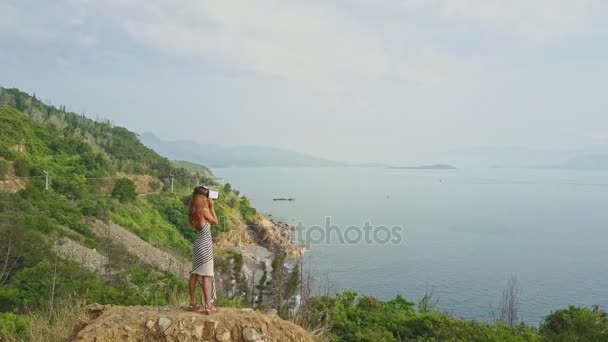 Девушка в шлеме виртуальной реальности смотрит на морской пейзаж — стоковое видео