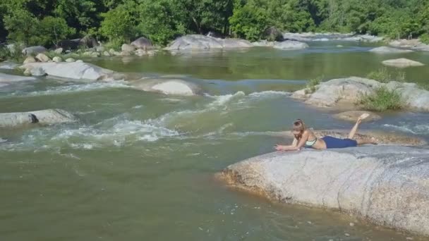 Девушка слушает музыку на камне в реке — стоковое видео