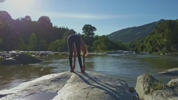 Holka dělá jógu na břehu řeky kamenné — Stock video