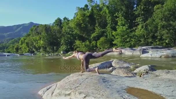 Meisje doet yoga op stenen rivier bank — Stockvideo