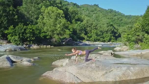 Chica haciendo yoga en piedra ribera del río — Vídeo de stock