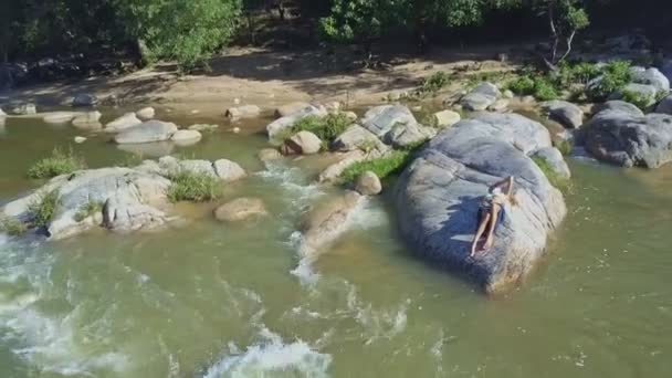 Дівчина лежить на камені серед річкових порогів — стокове відео