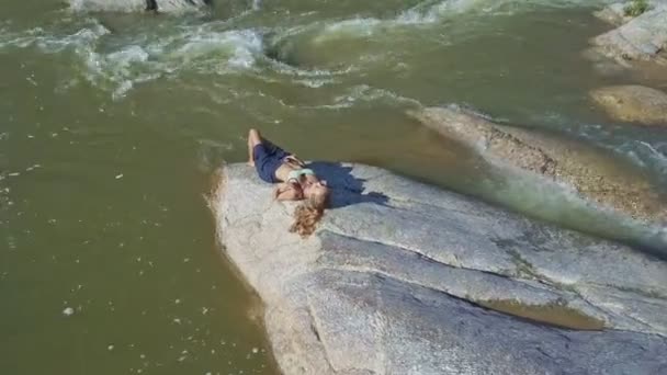 Chica acostada en piedra entre los rápidos del río — Vídeo de stock