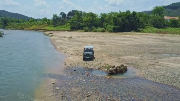 Jeep militaire conduite sur gravier près de la rivière — Video
