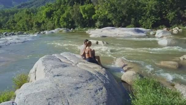 Casal senta-se na rocha entre rio de streaming — Vídeo de Stock