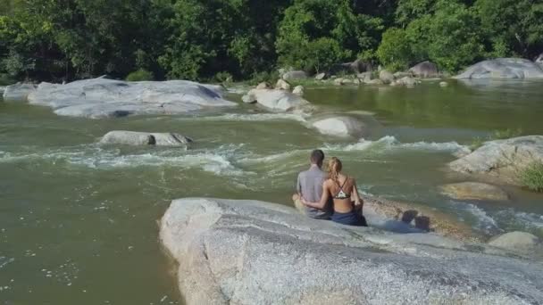 Casal senta-se na rocha entre rio de streaming — Vídeo de Stock