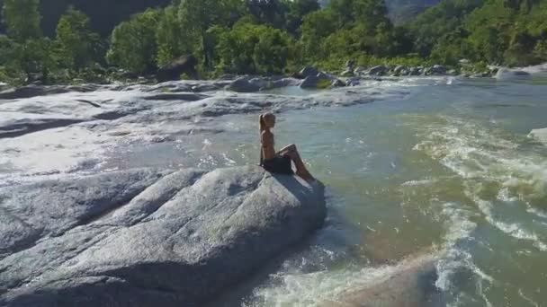 Девушка, сидящая на камне среди речных порогов — стоковое видео