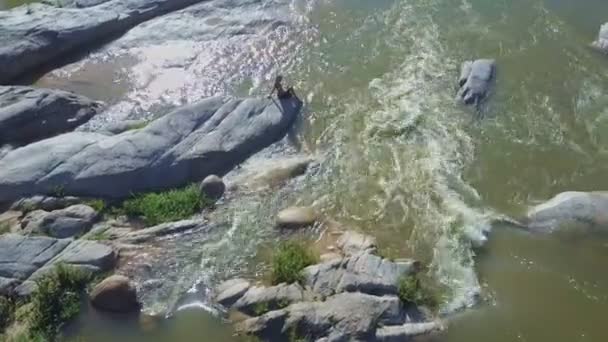 Dziewczyna siedzi na kamieniu wśród rwących rzek — Wideo stockowe