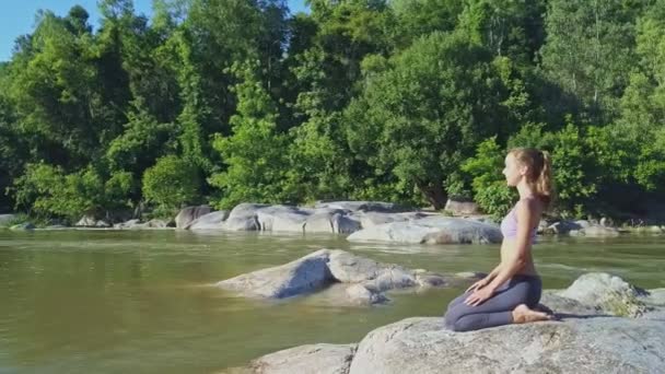 Девушка, занимающаяся йогой на берегу каменной реки — стоковое видео
