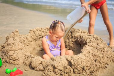 Sahilde kum yığını arasında kız oturur