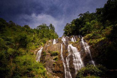 sarp kayalık uçurum sonsuz derin mavi gökyüzü altında orman arasına gizlenen akışlarında resimsel yüksek şelale