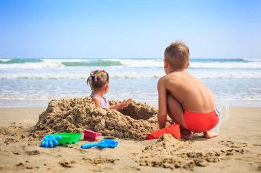 Kız ve erkek sahilde kum yığını tarafından oturmak