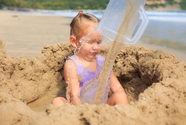 Plajda su arkasında kum deliğe kız oturuyor