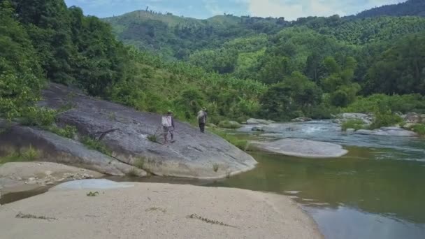Мужчины гуляют по скальному берегу реки — стоковое видео