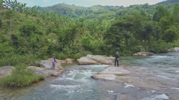 Männer gehen auf felsigem Ufer über Fluss — Stockvideo