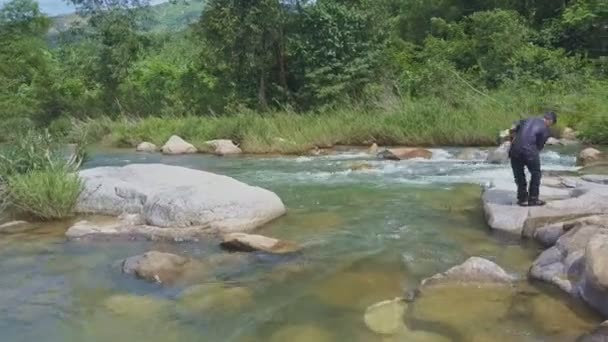Человек стоит на плоском камне среди реки — стоковое видео