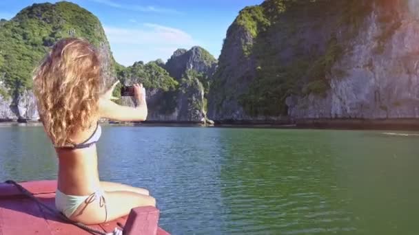 摄像头显示侧面视图苗条性感长发女孩在比基尼使自拍反对平静蔚蓝海湾由巨大陡峭的岩石 — 图库视频影像