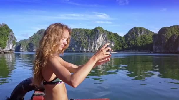 性感长发女孩微笑 使自拍在船上弓反对图案蔚蓝的海洋海湾和巨大的陡峭的岩石 — 图库视频影像