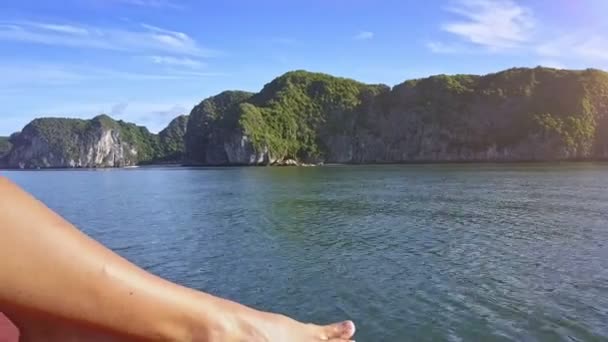 クローズ アップ長いセクシーな女の子の脚と足の静かな湾の紺碧水と岩だらけの島の鎖のボートに乗って移動 — ストック動画