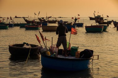 MUI KD/Vietnam - 17 Mart 2016: balıkçı duruyor Vietnamca bayrakları ve diğer balıkçı tekneleri karşı farklı eşya ile yuvarlak tekne günbatımında 17 Mart MUI Ne içinde