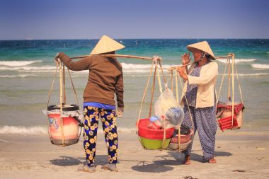 Nha Trang/Vietnam - 16 Nisan 2017: Vietnam şapka içinde yerel satıcılar boyunduruğu potalara mal ile konuşmak dalgaları karşı kum okyanus plaj üzerinde 16 Nisan Nha Trang içinde