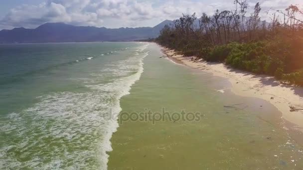 drone se déplace le long de la plage de sable lavé par l'océan azur longues et larges vagues mousseuses contre paysage tropical avec des collines 