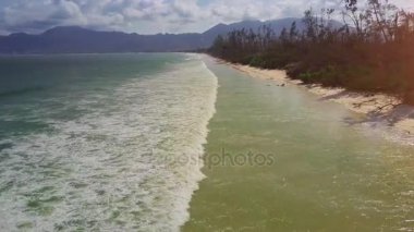 masmavi okyanus sörf kum plaj ve tropikal bitki karşı tepeler boyunca geniş dalgalar ile yakın dron taşır