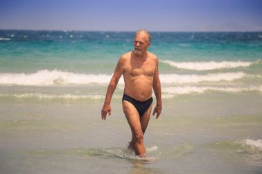 masmavi deniz köpüklü dalgalara karşı dalga sörf dışında closeup güçlü tabaklanmış sakallı yaşlı adam yürüyor