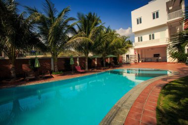 Mavi şeffaf su yüzme havuzu tarafından yan yolları beyaz otel binası yakınındaki palmiye ağaçları ile