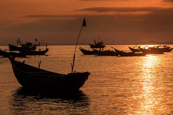 Vietnamese fishing boat silhouette with flagstaff in sea at bright sunset reflection on surface